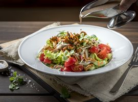 Ein bunter Salat im Restaurant Ayinger wird mit einem hellen Dressing beträufelt.