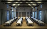 Ein großer Festsaal mit langen Vorhängen, vier Tischen und grauen Stühlen in der Eventlocation München