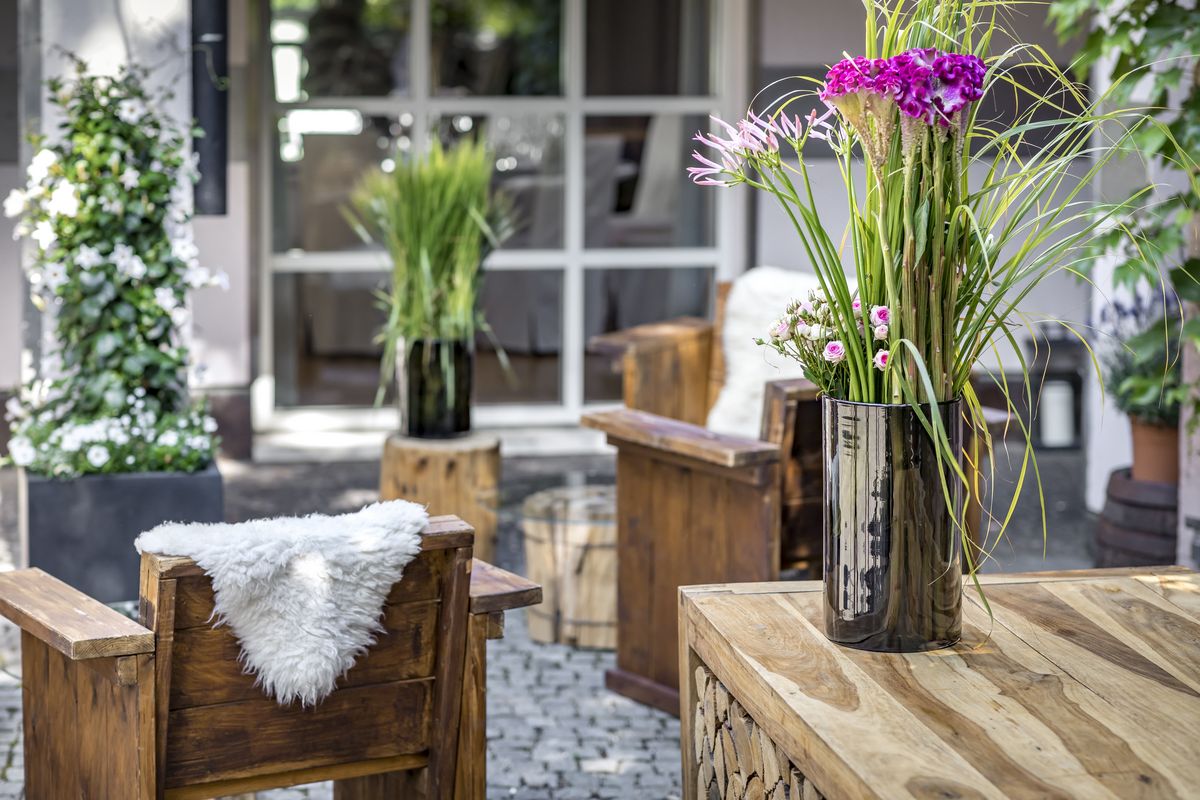 Außenbereich mit hölzernen Stühlen und schönen Blumenvasen mit violetten Blumen und steinernem Untergrund in der Eventlocation München