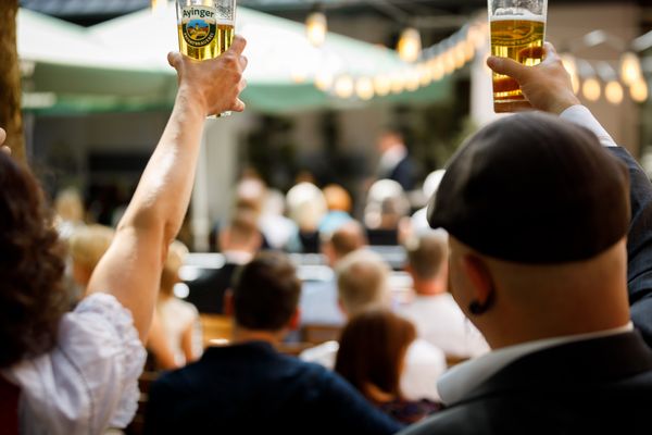 Menschen von hinten, die Biergläser in der Luft halten, wahrscheinlich bei einer privaten Feier in München